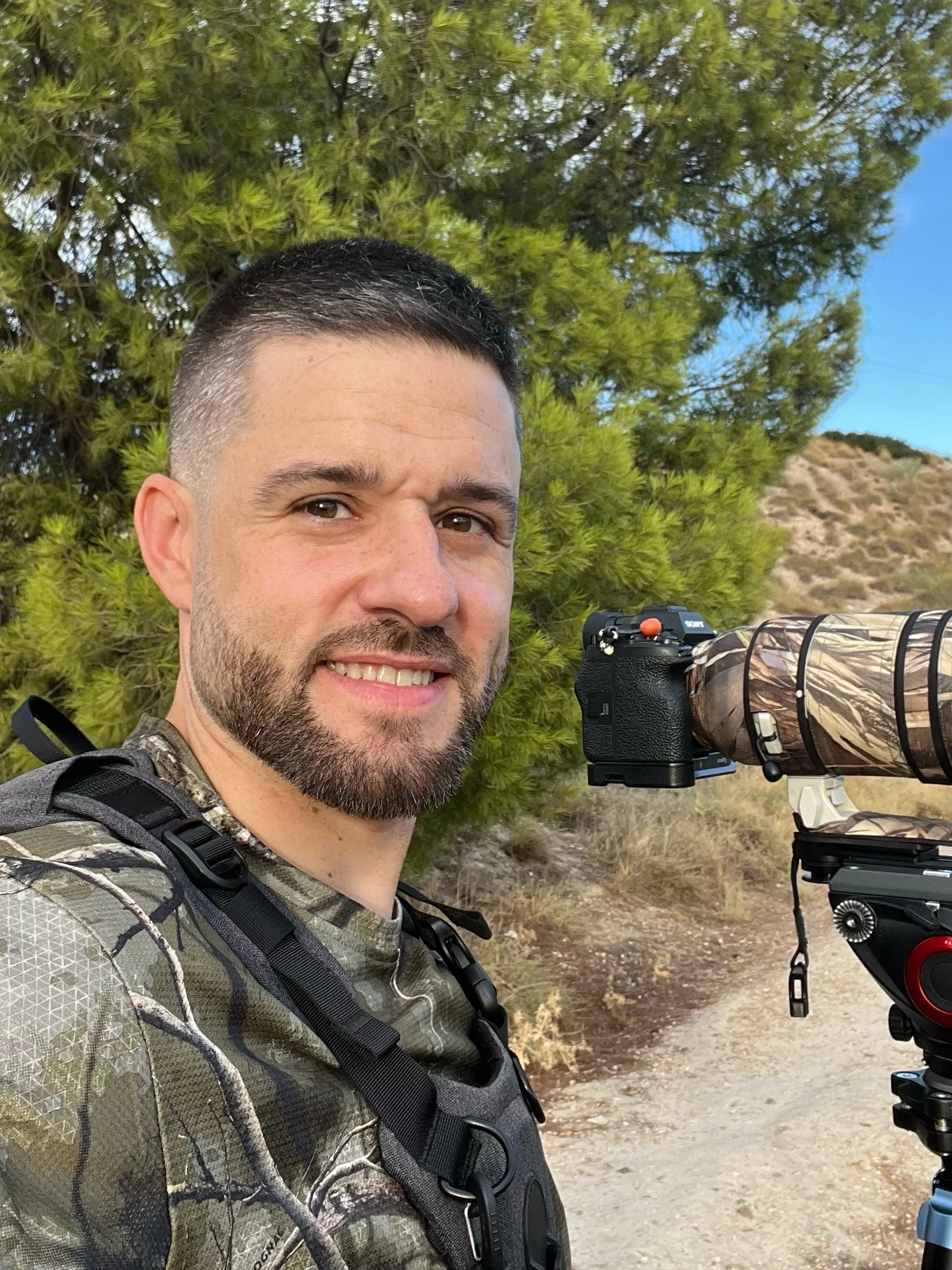 Retrato de Gabriel García al aire libre junto a una cámara con teleobjetivo montada sobre un trípode.